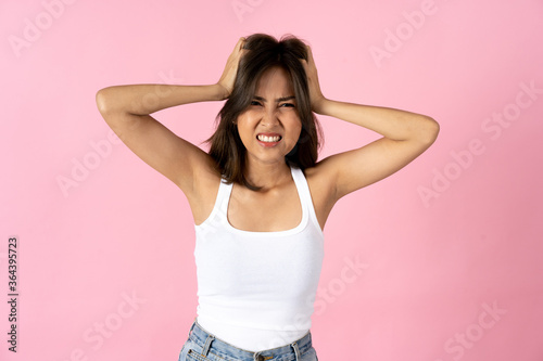Frustrated young woman looking at camera with hands in hair plain pink background