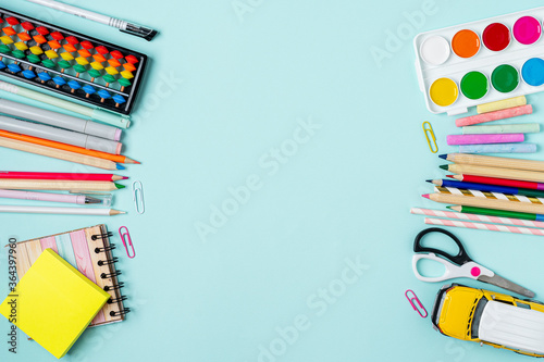 Flat lay of modern bright blue office desktop with school supplies on table around empty space for text. Top view Back to school concept