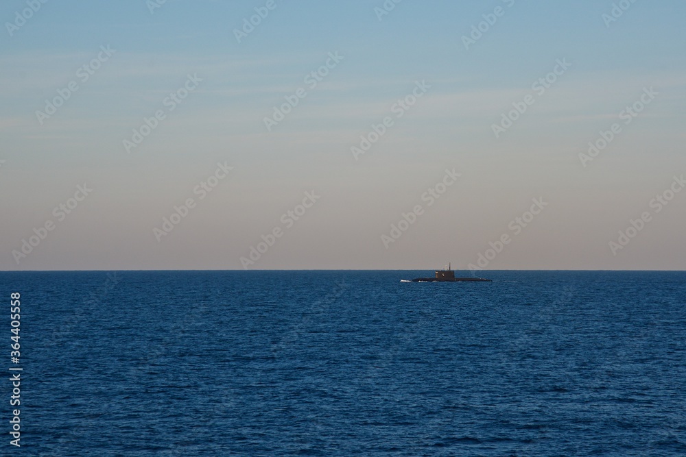 The submarine is surfaced in the open sea in the early morning. Seascape. Clear sky over the dark blue sea.
