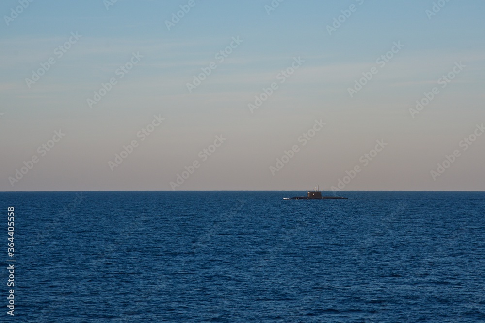 The submarine is surfaced in the open sea in the early morning. Seascape. Clear sky over the dark blue sea. The submarine is surfaced in the open sea in the early morning. Seascape. Clear sky over the dark blue sea.