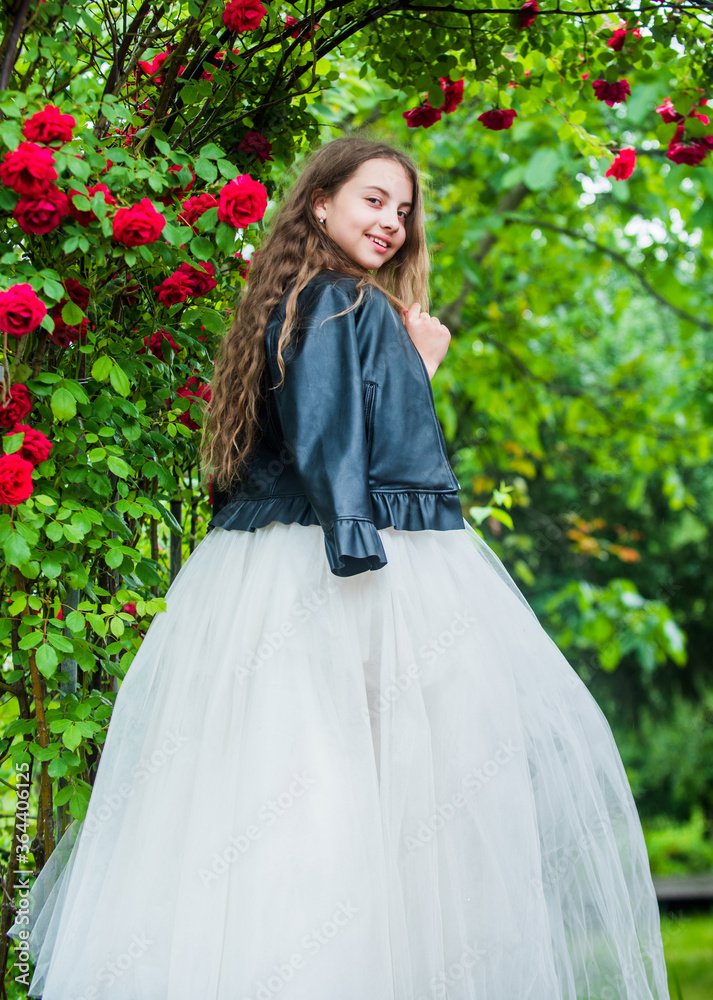 What a lovely dress. beauty and fashion. pretty kid smell rose flower. spring and summer nature. little girl in garden. child enjoy blossom in park. small cute lady in leather jacket. happy childhood