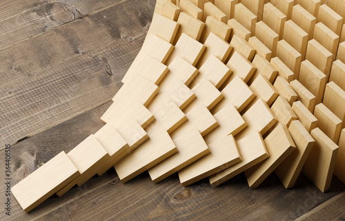 Wooden domino stones pyramid on wood floor falling over, chain reaction or multiplication effect concept photo