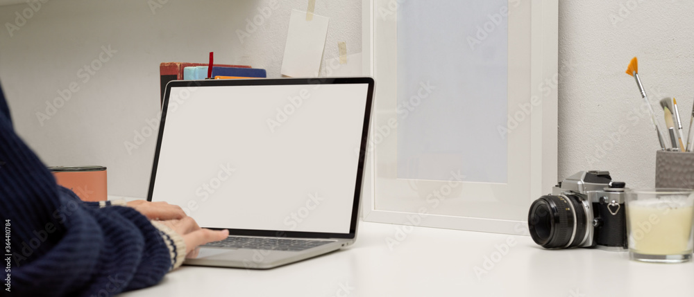 Female working with mock up laptop on white table with painting tools, decorations and camera
