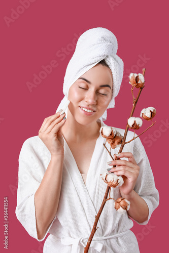 Beautiful young woman with cotton flowers and cosmetic pad on color background