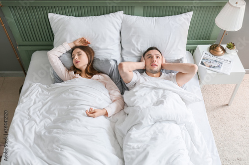 Young irritated man in bed with snoring wife