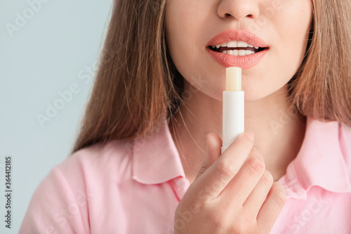 Beautiful young woman with lip balm on light background, closeup