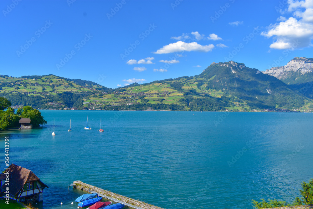 Magnificent view of lake Thun and the Alps, Switzerland. Blue sky, blue water, boats, green trees. Sunny summer weather.