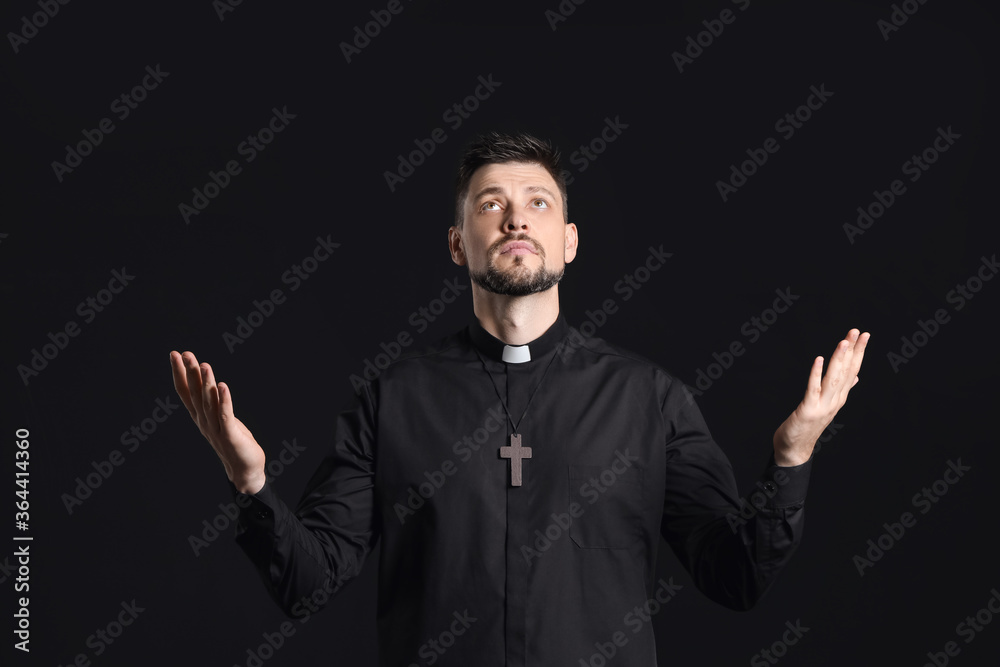 Handsome praying priest on dark background Handsome praying priest on dark background