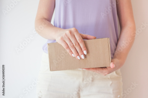 Beautiful girl with a parcel in hands, delivery concept. White manicure, box with order © Natali