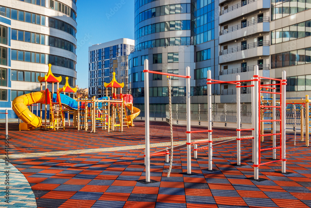 The sunny children's playground among modern futuristic buildings. A luck of natural environment in a city concept The sunny children's playground among modern futuristic buildings. A luck of natural environment in a city concept