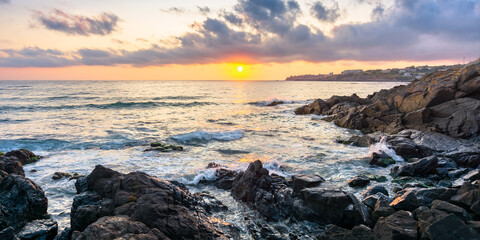 Leinwandbilder Schwarz coast of the ocean at sunset. beautiful landscape with rocks in the water. gorgeous cloudscape above the sun and horizon. concept of calmness and mediatation  © Pellinni