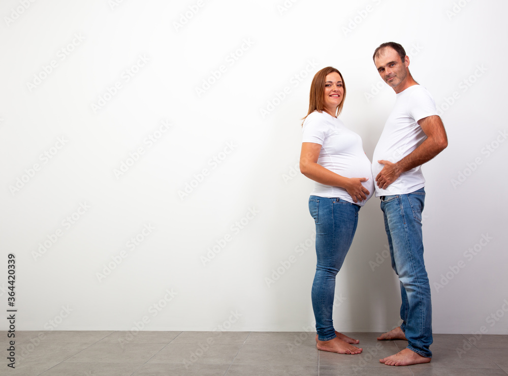 Pregnancy. Happy Family Expecting Baby. Man and a pregnant woman are measured by bellies. Funny full length portrait of wife and husband at home. Couple lifestyle Pregnancy. Happy Family Expecting Baby. Man and a pregnant woman are measured by bellies. Funny full length portrait of wife and husband at home. Couple lifestyle