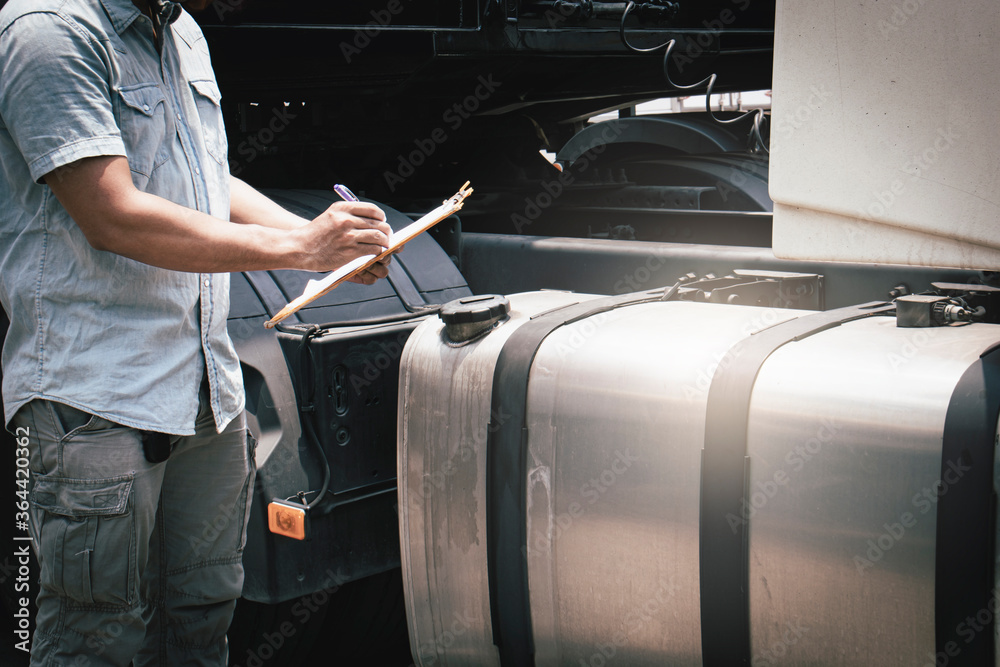 A truck driver holding clipboard safety checking a large fuel tank of semi truck. A truck driver holding clipboard safety checking a large fuel tank of semi truck.
