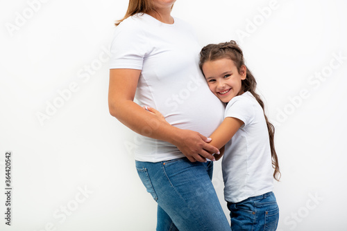 Pregnancy. Happy Family Expecting Baby. Beautiful smiling girl hugs her pregnant mother with big belly. Indoor portrait of mom and daughter. photo