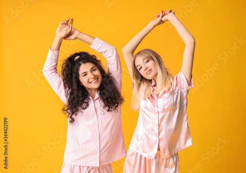Beautiful young women in pajamas on color background