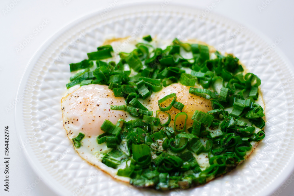 Fried eggs with green onions on a white plate.Breakfast with eggs. Fried eggs with green onions on a white plate.Breakfast with eggs.