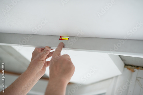 Obraz na plátně Tool level in men's hands and a flat horizontal surface of the ceiling