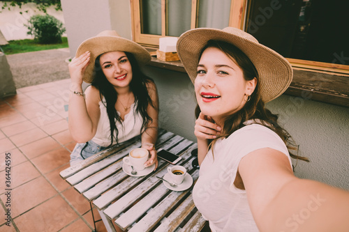 Cheerful young ladies take coffee break at the table bar and do selfie picture - people in holiday vacation or friends in outdoor leisure activity together drinking and enjoying the day photo