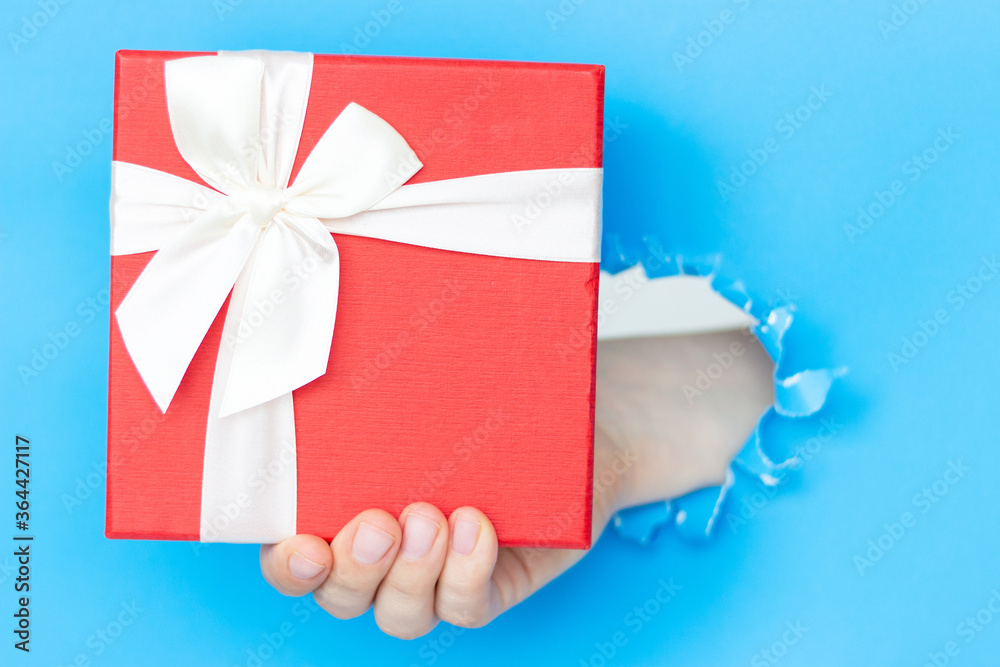 A woman's hand holds a gift with a white bow on blue background A woman's hand holds a gift with a white bow on blue background