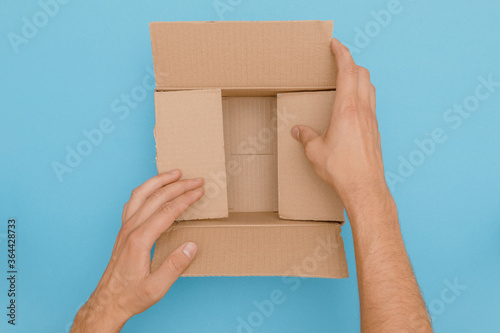 Canvas Print Hands fold empty cardboard box ready to deliver as package on blue background