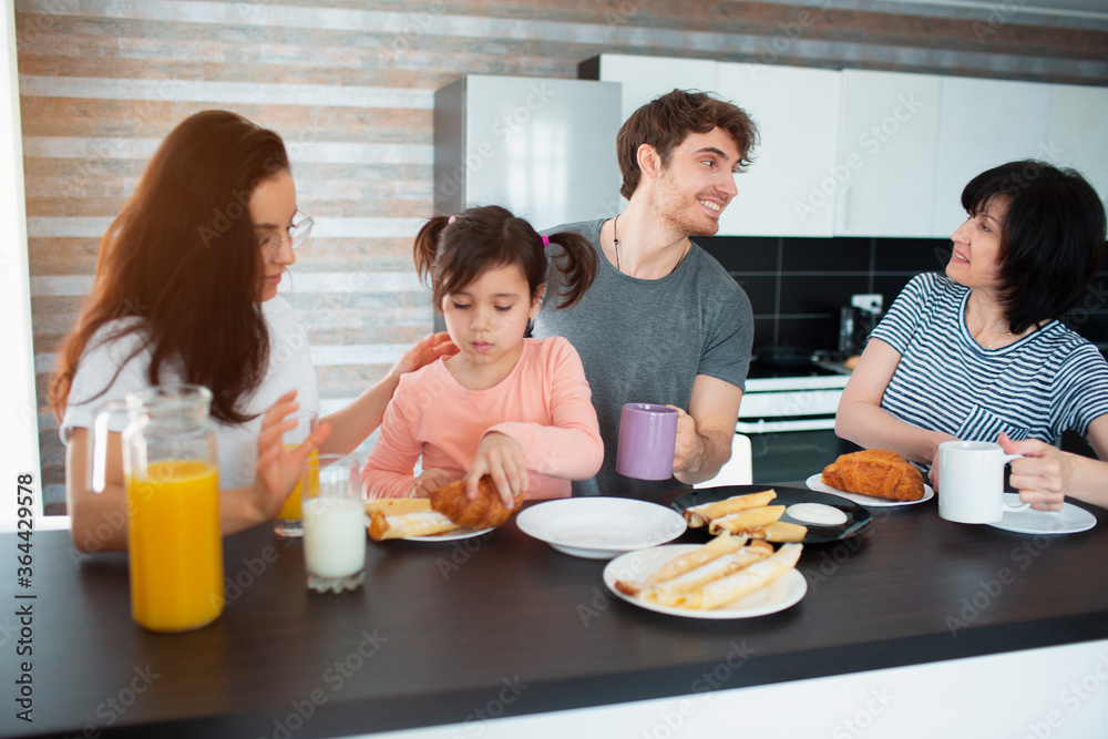 Happy breakfast of a large family in the kitchen. Siblings, parents and children, mother and grandmother. Father and daughter. Everyone is eating in the morning and chatting and having fun. Happy breakfast of a large family in the kitchen. Siblings, parents and children, mother and grandmother. Father and daughter. Everyone is eating in the morning and chatting and having fun.