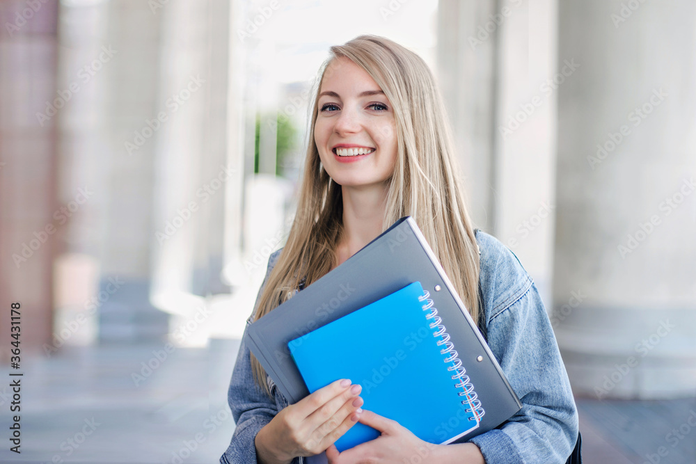 Female student outdoors holding a notebook and smiling Female student outdoors holding a notebook and smiling
