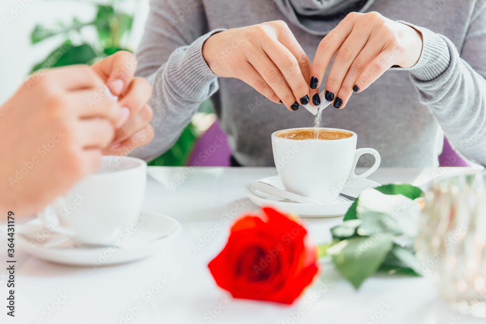 Cropped photo of female and male hands pouring sugar into coffee, dating at the table in a cafe shop. Cropped photo of female and male hands pouring sugar into coffee, dating at the table in a cafe shop.