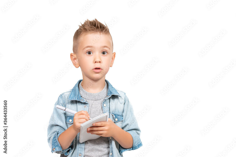Cute attentive little boy looking at camera writing something in her notebook Cute attentive little boy looking at camera writing something in her notebook