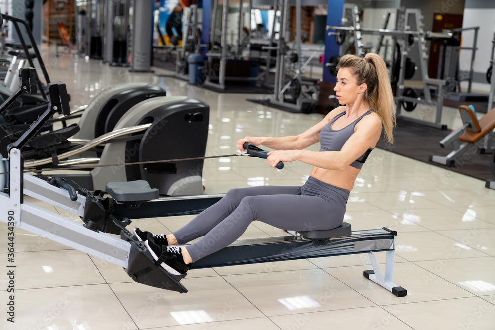 Young woman working out on row machine at gym exercising Young woman working out on row machine at gym exercising