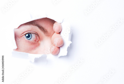 Fotografie Mans blue eye peering through through ripped paper