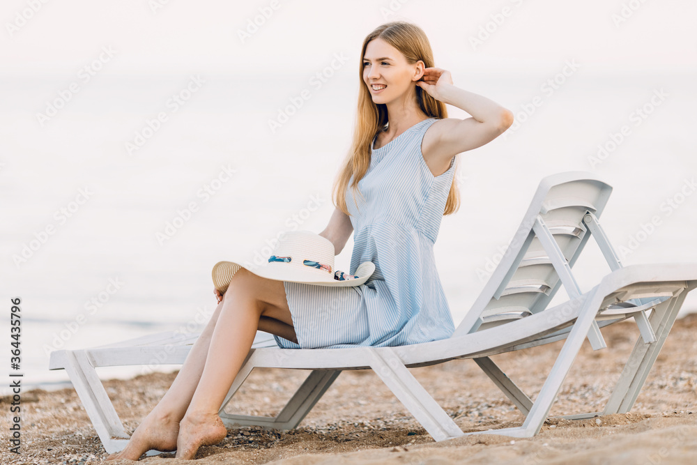 Relaxing beautiful girl in a summer dress, relaxing on a sandy beach, lying on a chaise longue. Summer vacation, travel, sea