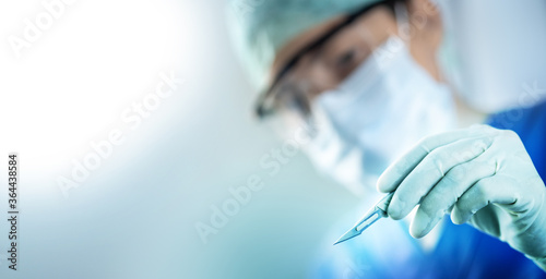 Fotografiet close up of the surgeon's hand holding a scalpel and blurred female doctor's fac