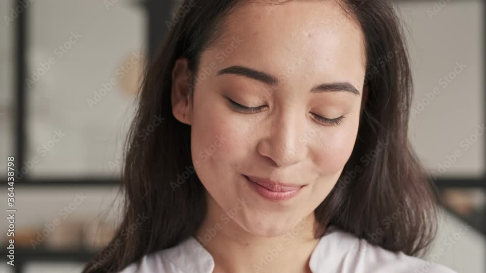 Close up view of Smiling elegant pretty asian woman becoming shy and looking at the camera at home Close up view of Smiling elegant pretty asian woman becoming shy and looking at the camera at home