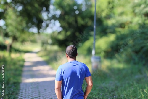 close portrait of young man in blue t shirt standing outside in park with trees in background