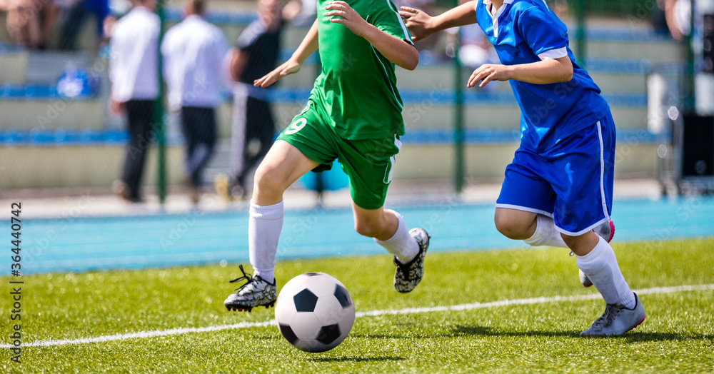 Obraz premium Football Players in Running Duel. Forward and Defense Player Compete for the Ball. Sports Stadium in the Background