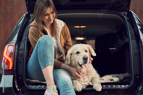 Young woman with golden retriever sit in open trunk of black car