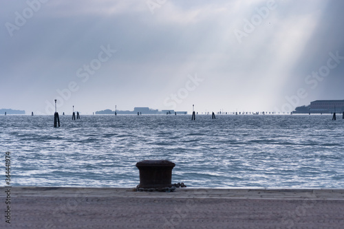 The lagoon of Venice on a rainy and cold day. No people around, no boats around, just a great cloudy sky whits sunlight seeping through and water