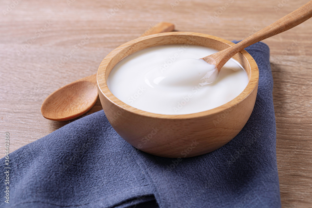 Yogurt in wooden bowl with spoon and blue cotton on table background . Yogurt in wooden bowl with spoon and blue cotton on table background .