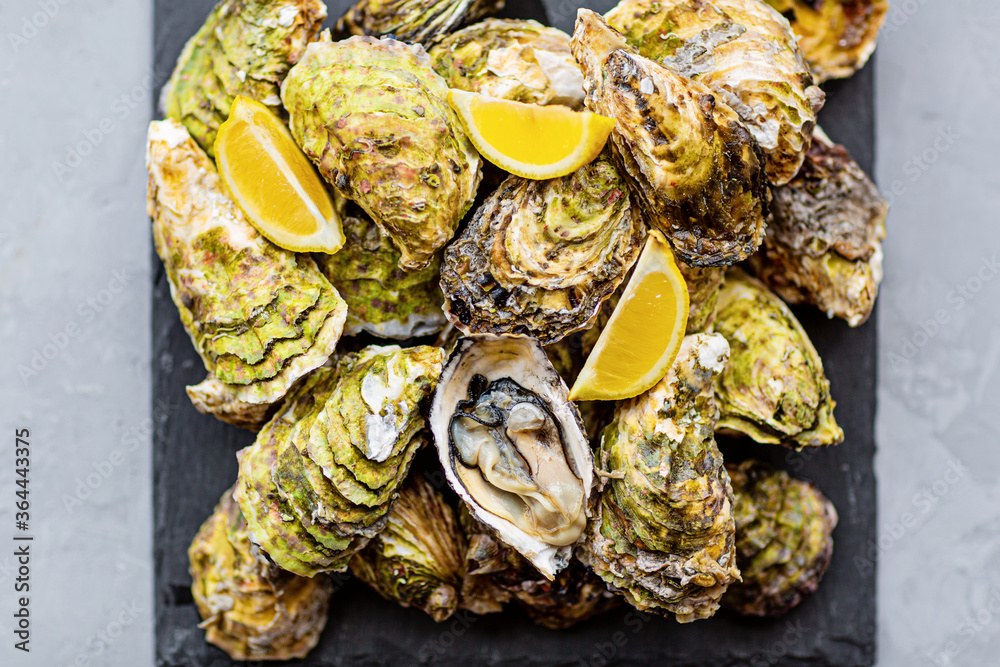 Fresh opened Oysters close-up on black plate with sliced lemon and ice. Healthy sea food. Gourmet food. Flat lay, top view, mockup, overhead, template with copy space. Online order and food delivery Fresh opened Oysters close-up on black plate with sliced lemon and ice. Healthy sea food. Gourmet food. Flat lay, top view, mockup, overhead, template with copy space. Online order and food delivery