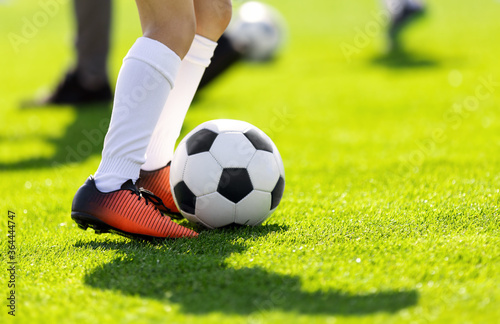 A young man kicking a football outdoors. Young football players training on a grass field. Boys in a sportswear. Soccer players wearing white socks and soccer boots. Football horizontal background