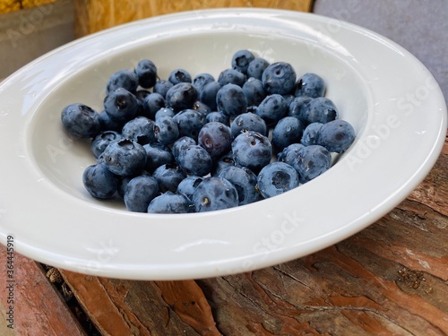 The blueberry is on the white plate on the wood