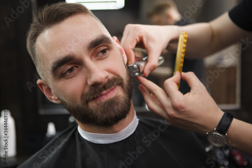 Handsome man smiling while barber trimming his beard