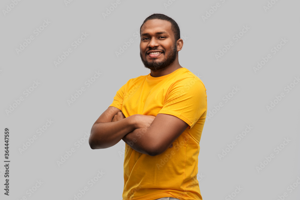 people concept - smiling young african american man in yellow t-shirt with crossed arms over grey background