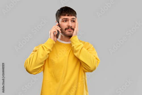 technology and people concept - sad young man in yellow sweatshirt calling on smartphone over grey background