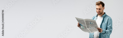smiling young man reading newspaper isolated on grey, panoramic shot