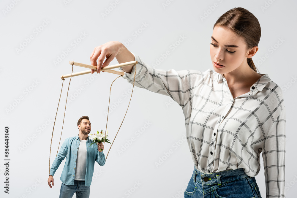 female puppeteer holding male marionette with flowers isolated on grey female puppeteer holding male marionette with flowers isolated on grey