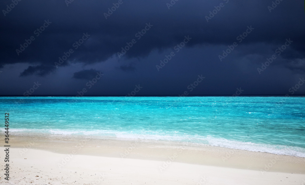 Tropical Maldives beach with turquoise blue water and rain sky.