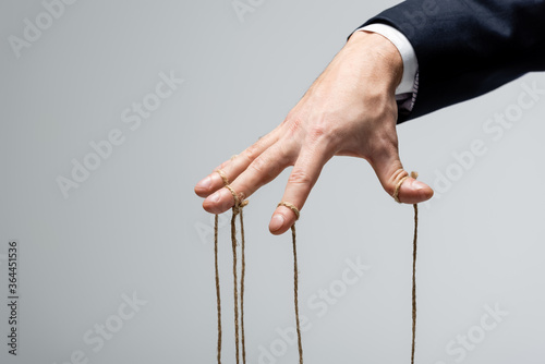 partial view of puppeteer in suit with strings on fingers isolated on grey photo