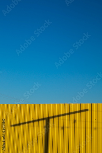 background image clear blue sky yellow fence where the shadow of the post is a play of light and shadows in the summer in Sunny weather outdoors