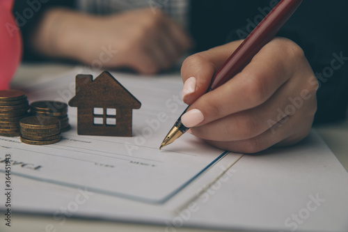 Close up wooden toy house with Woman signs a purchase contract or mortgage for a home, Real estate concept.